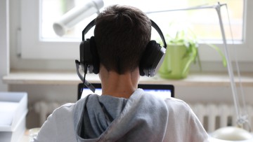Azubi im Homeoffice: Ein männlicher Azubi von hinten, wie er am Laptop sitzt und Kopfhörer trägt
