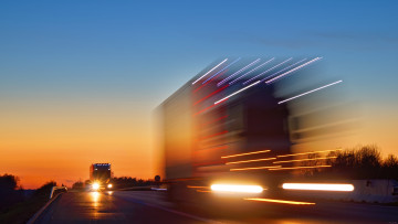Geschwindigkeitsüberraschungen verwischen entgegenkommende Lastwagen mit leuchtenden Lichtern auf der Autobahn nach Sonnenuntergang. Leuchten die Scheinwerferautos. Blauer und orange heller Himmel in der Abenddämmerung.