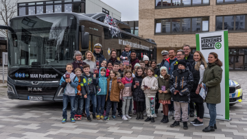Vor einem Bus stehen Grundschulkinder mit FC Bayern München-Legende Giovane Elber und Verkehrswacht-Experten.
