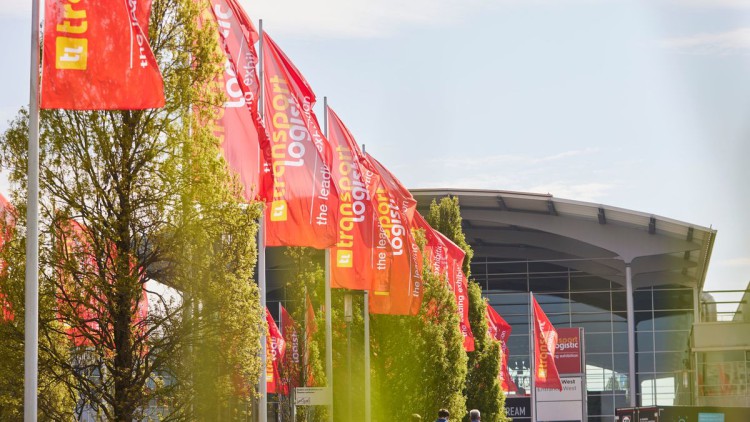 Der Eingangsbereich der Messe München. Davor wehen die roten Fahnen mit dem gelb-weißen Schriftzug der Messe transport logistik